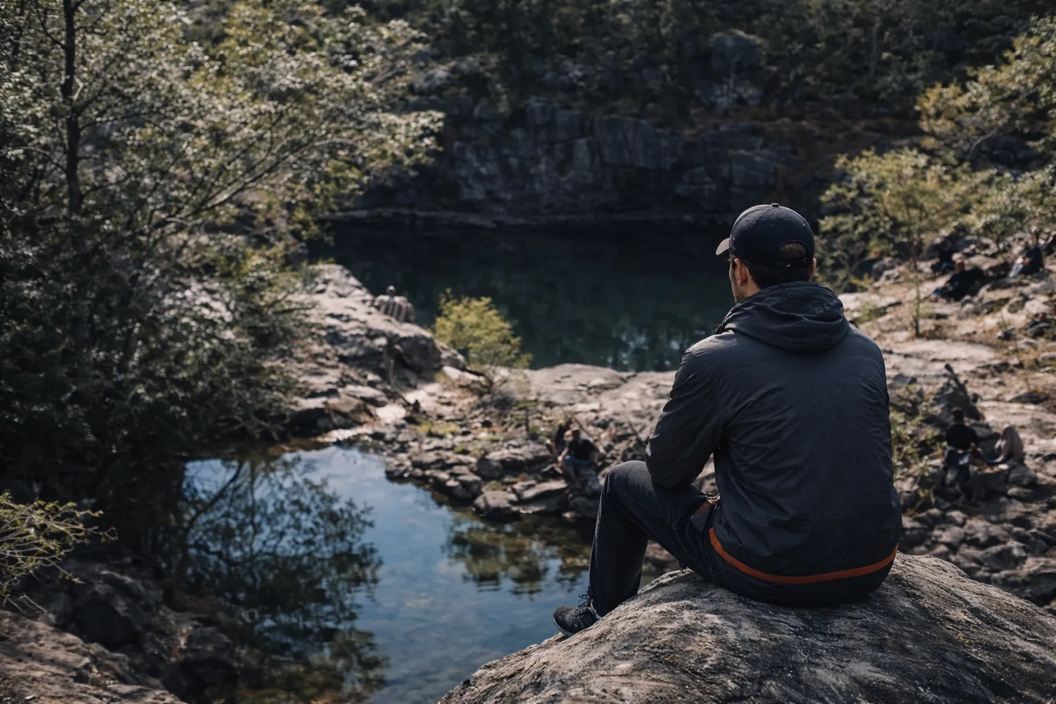 A young man sitting alone by a still lagoon, reflecting during Forged